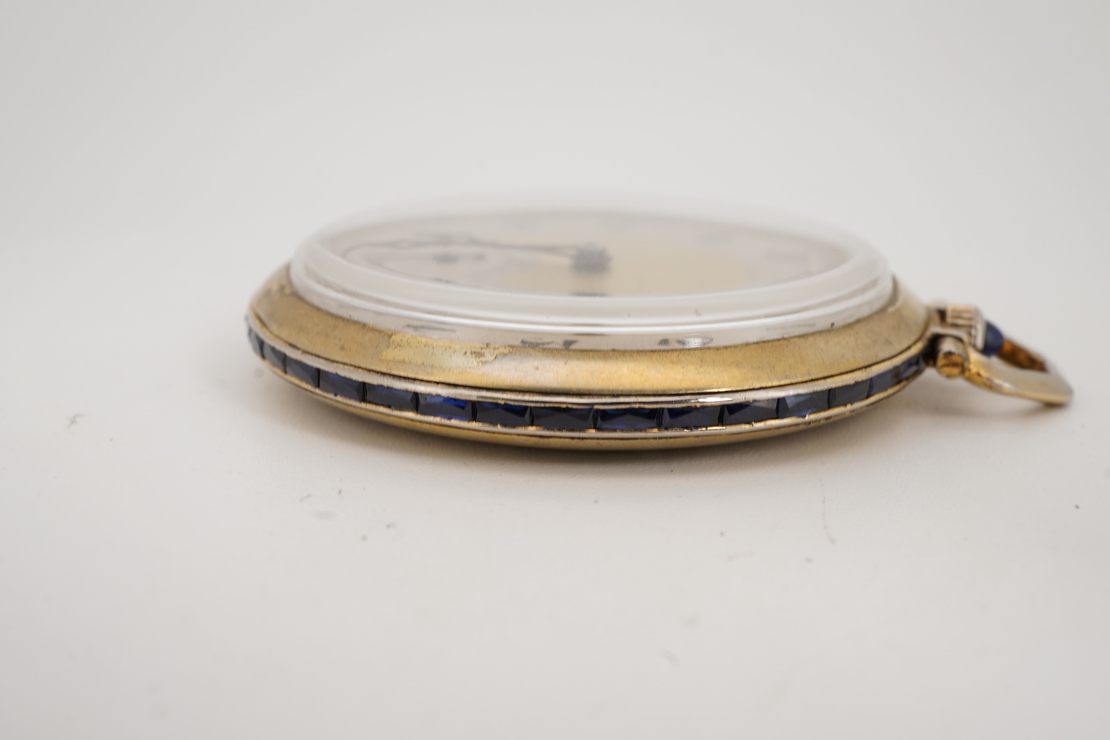 A French Art Deco parcel gilt white metal open faced dress pocket watch, with synthetic sapphire set border and winding crown